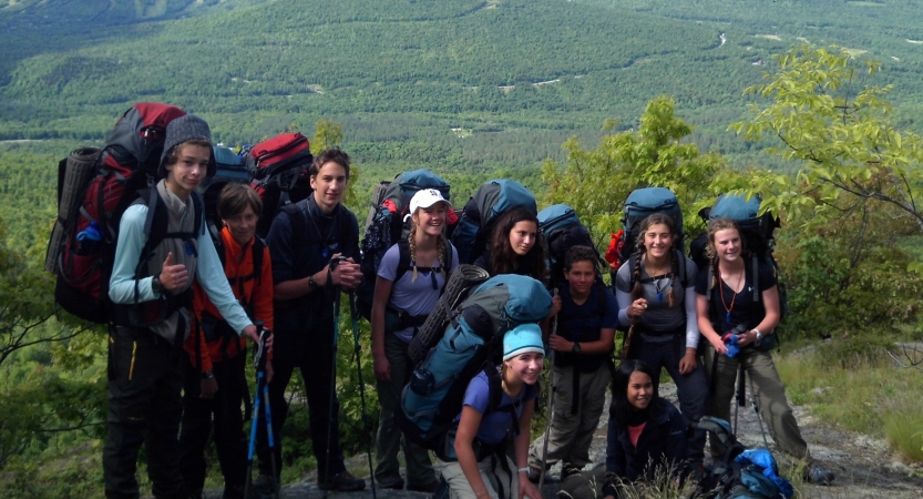 A group of backpackers pose for a photo in front of a green mountain lanscape